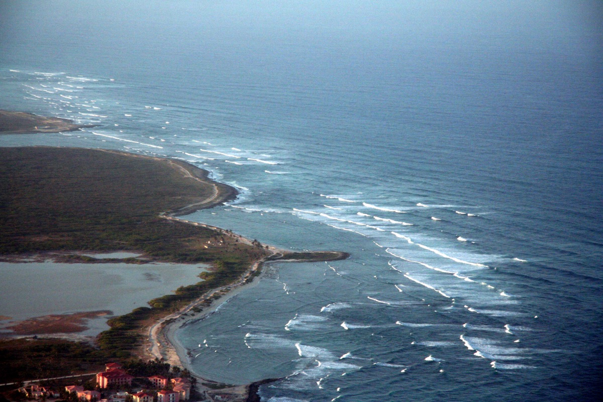 Vista aérea de la costa este: terrenos verdes que bajan hasta el arrecife y el mar.