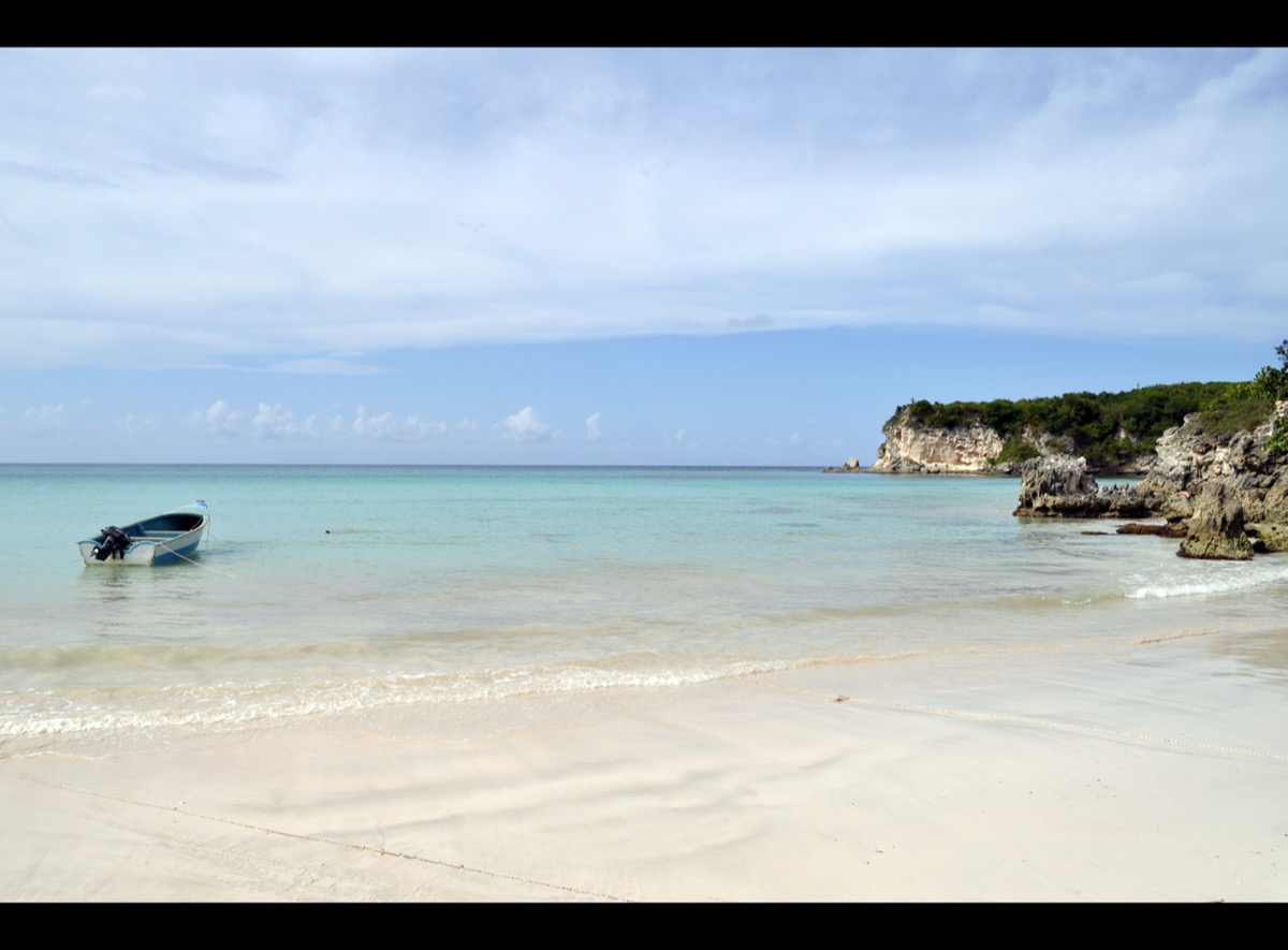 Playa Macao: agua turquesa y transparente, una lancha fondeada y acantilados cubiertos de vegetación.