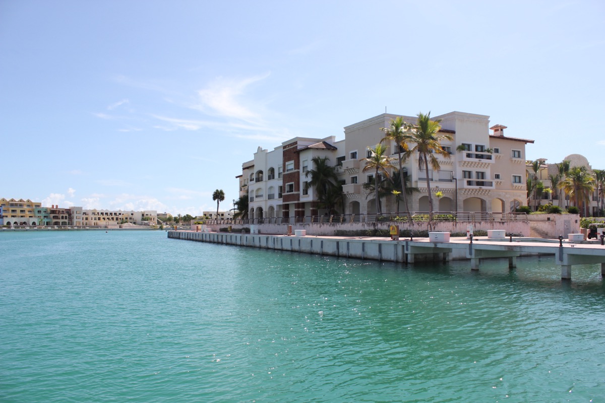 Marina de Cap Cana: edificios residenciales de tres y cuatro pisos con palmeras, junto a un canal de agua turquesa.