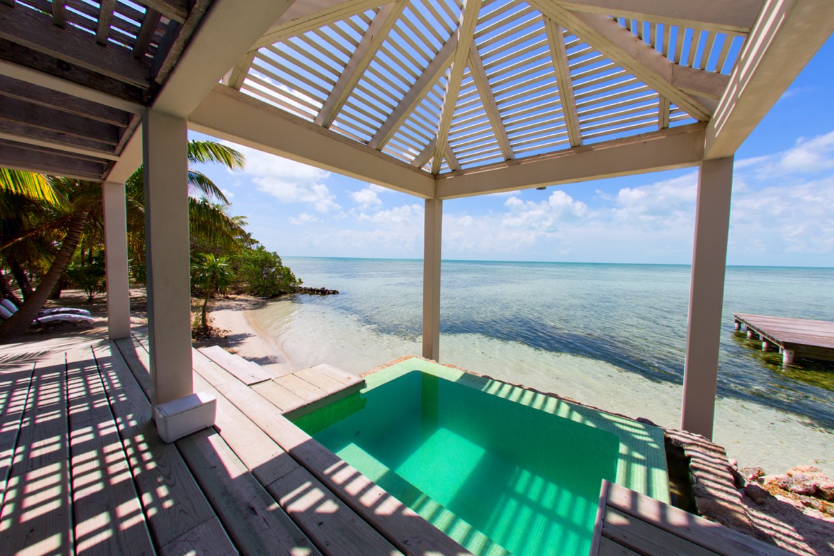 Terraza de madera con piscina privada bajo una pérgola blanca, abierta al mar.